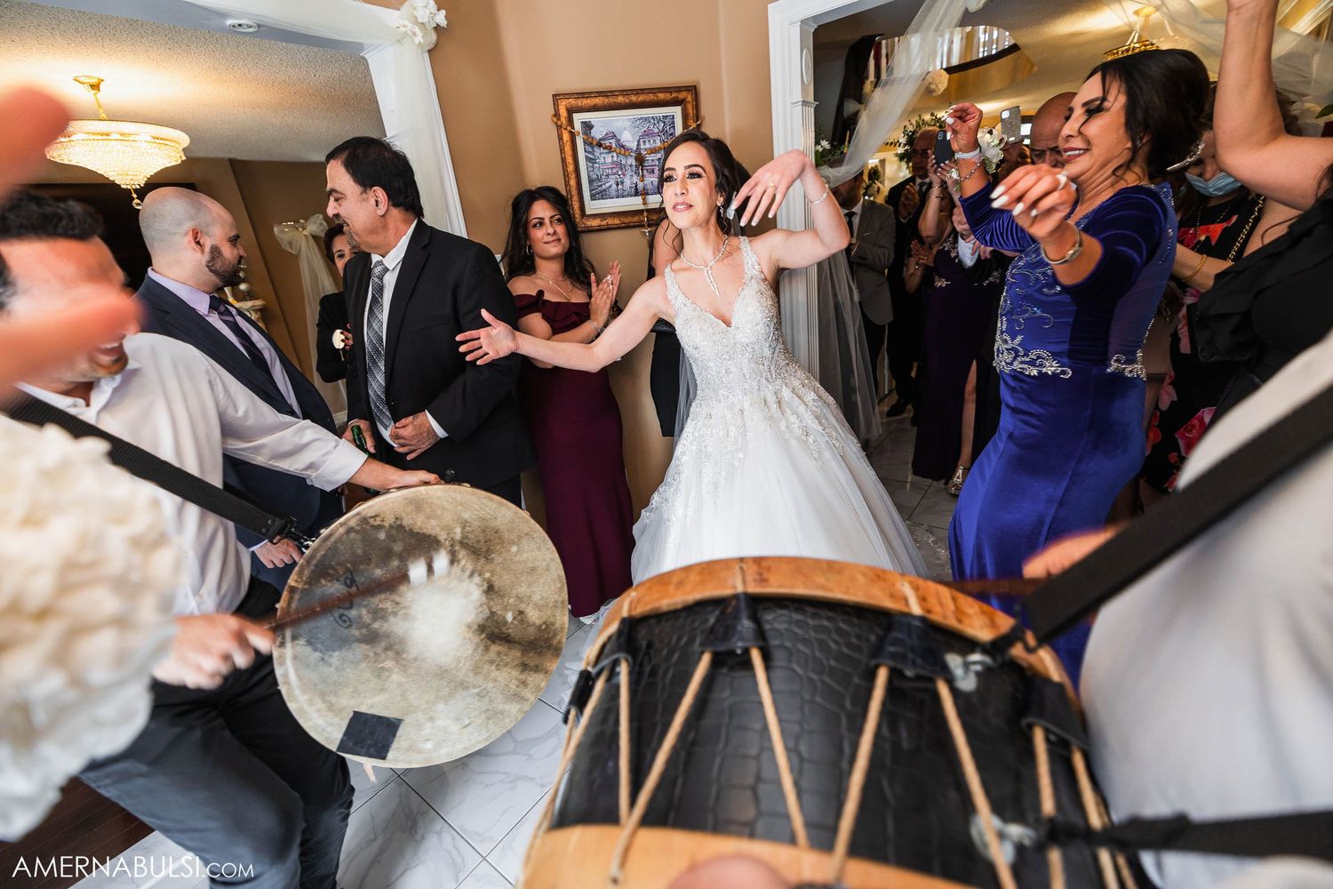 Wedding guests dancing and celebrating while musicians play traditional drums at an indoor reception.