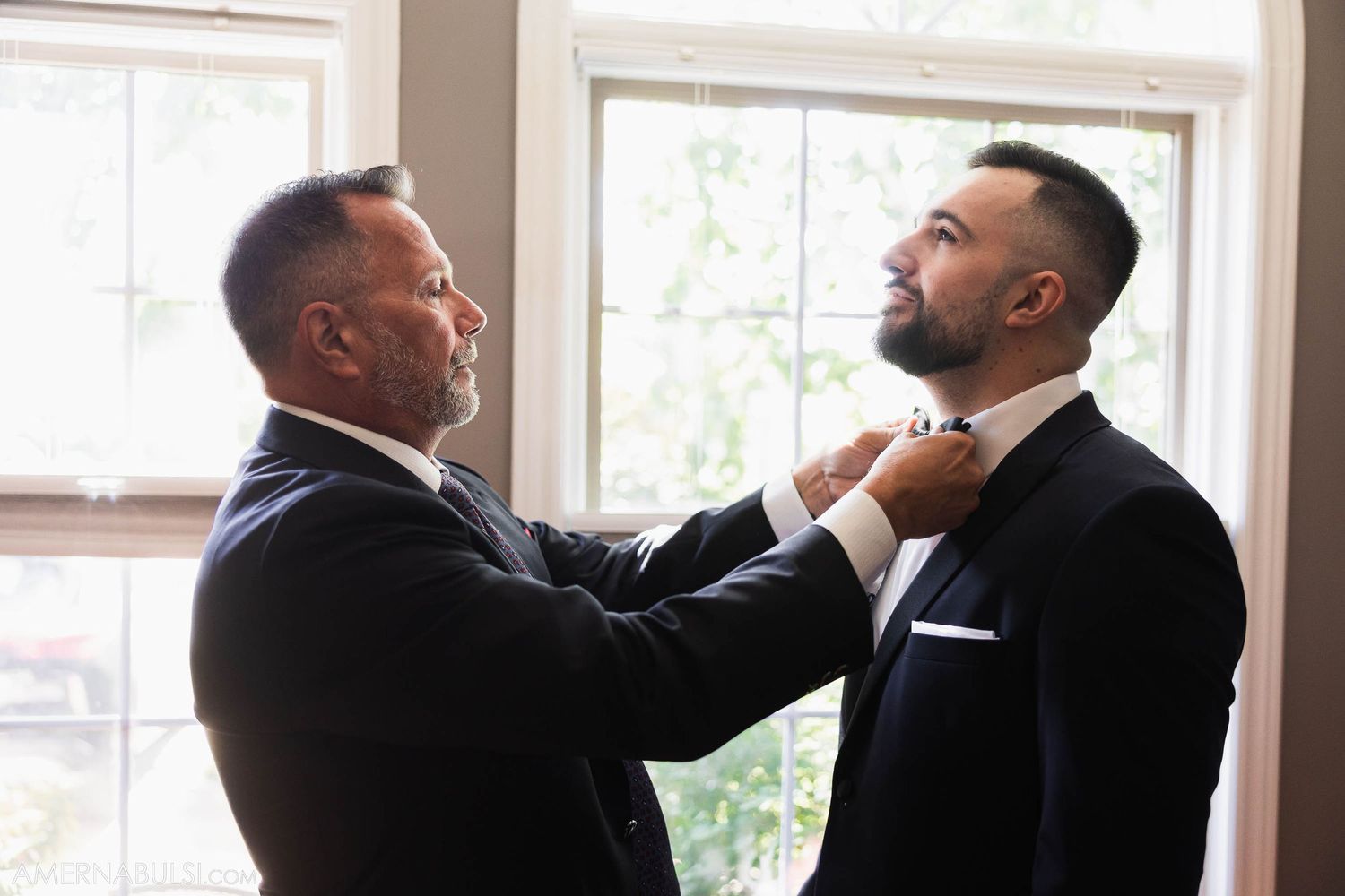Two people adjusting formal attire indoors during wedding preparation.