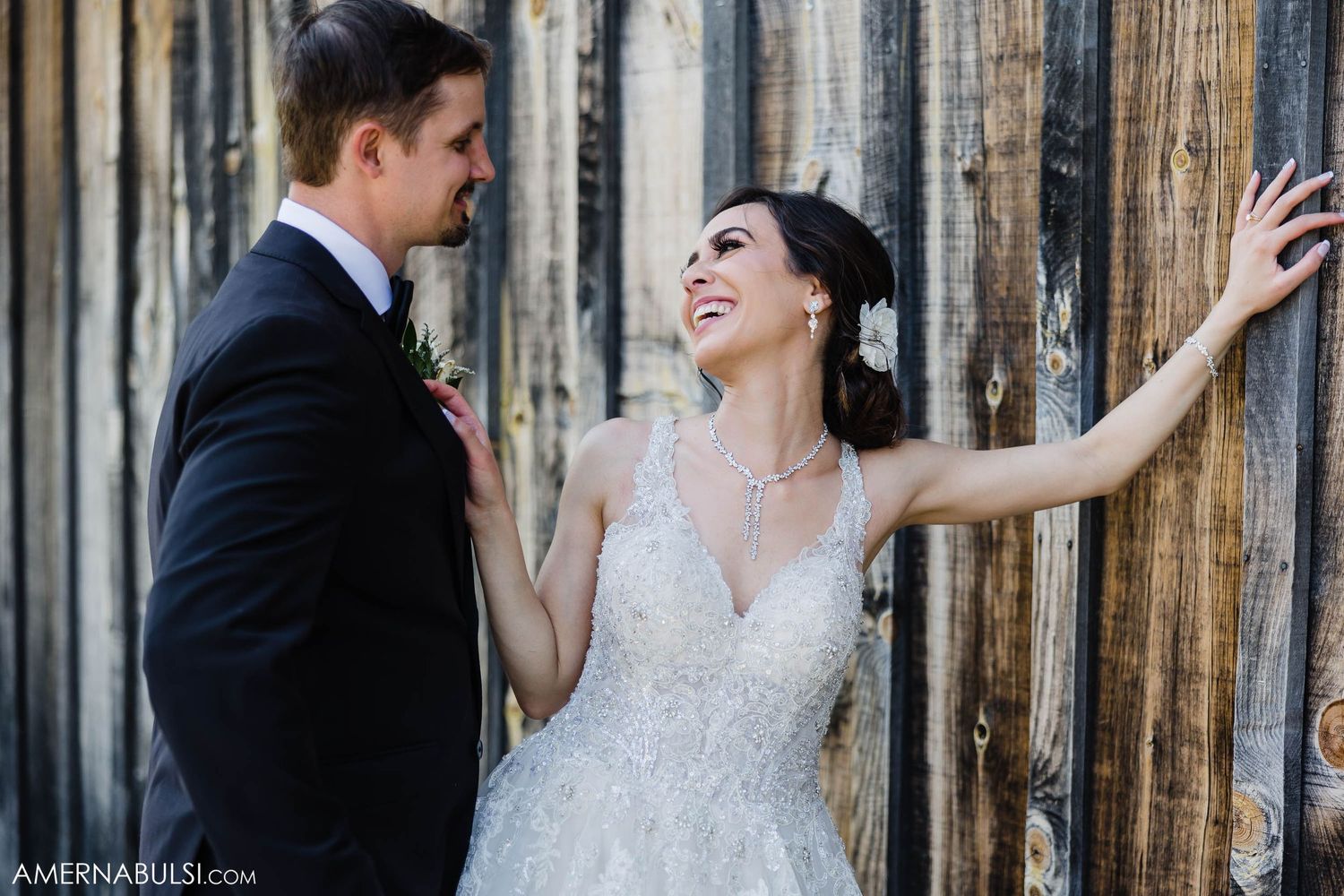 Joyful wedding moment with couple laughing against wooden wall background.