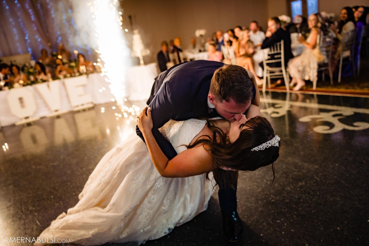 Dramatic dip during first dance with sparkler effects in background at wedding reception.