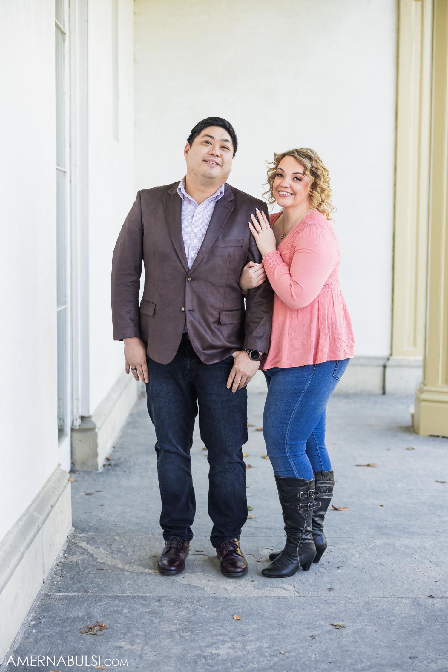 A couple poses playfully together on a porch with classical white columns.