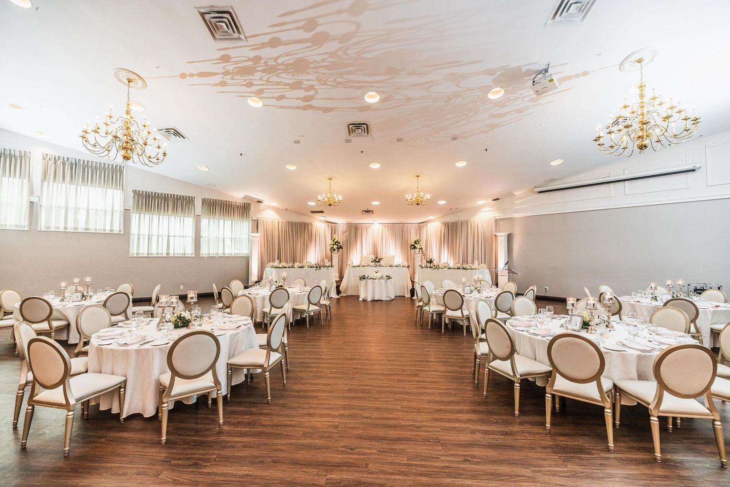 Elegant wedding reception venue with white decor, chandelier lighting, and round dining tables.