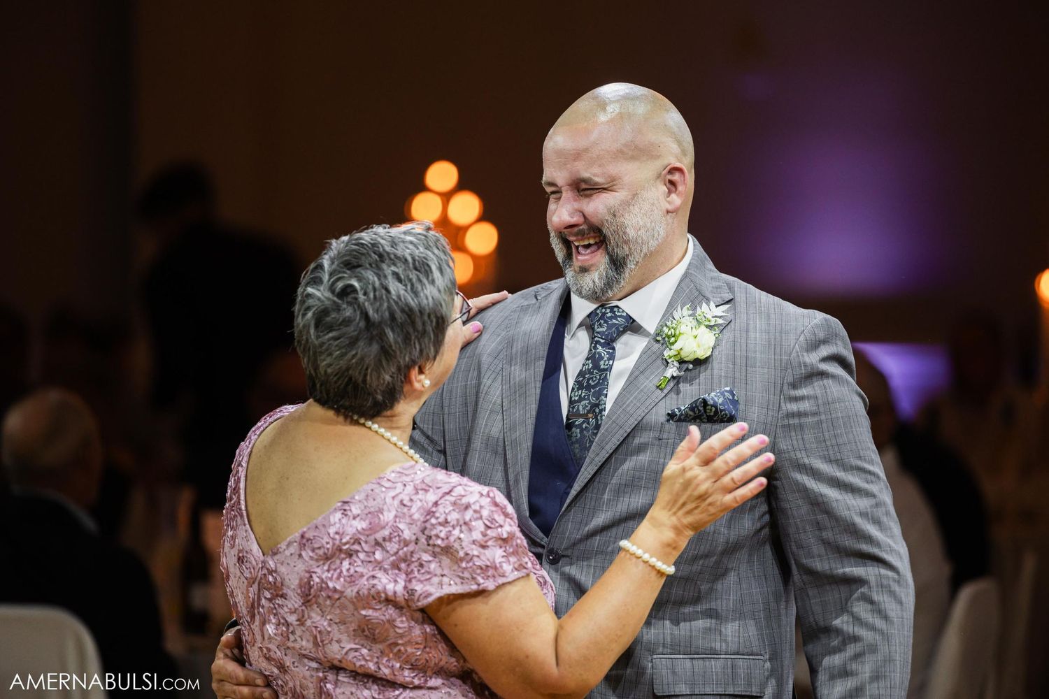 Tender moment between dancing couple at elegant reception with purple lighting.