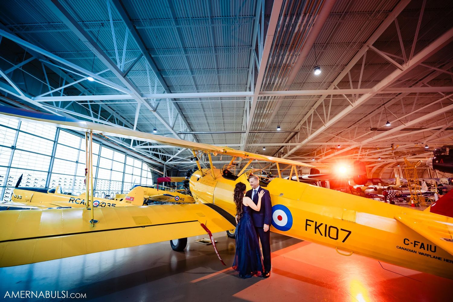 Couple posing in front of vintage yellow aircraft in museum hangar.