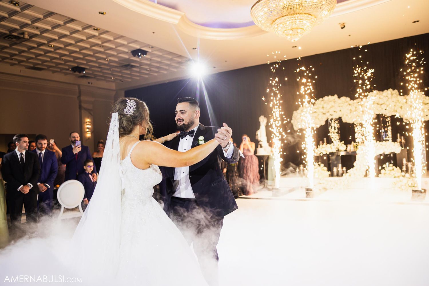 Couple performs first dance with pyrotechnic effects and fog on dance floor.