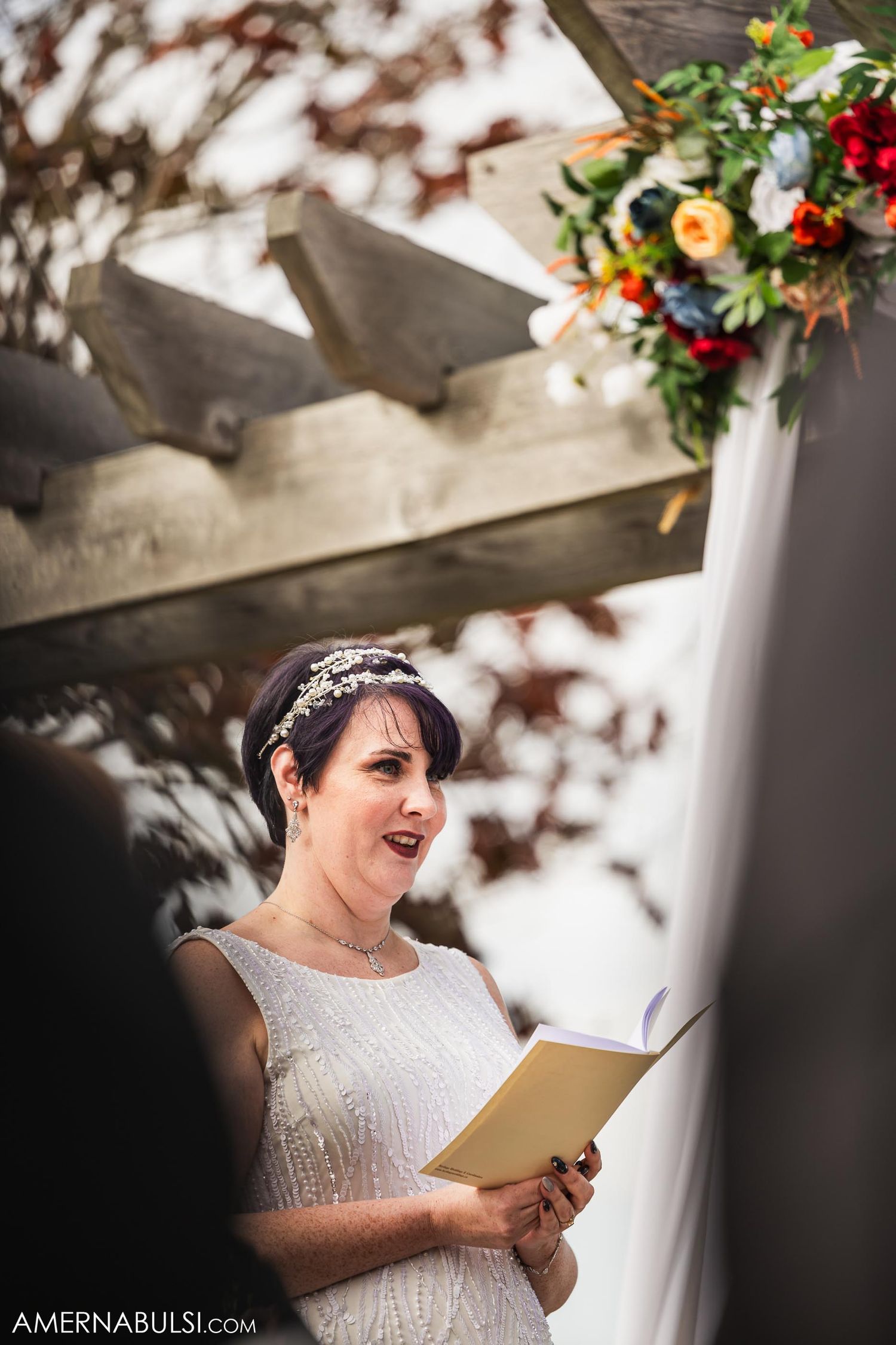 Candid moment of person in white dress reading from book during outdoor wedding ceremony.
