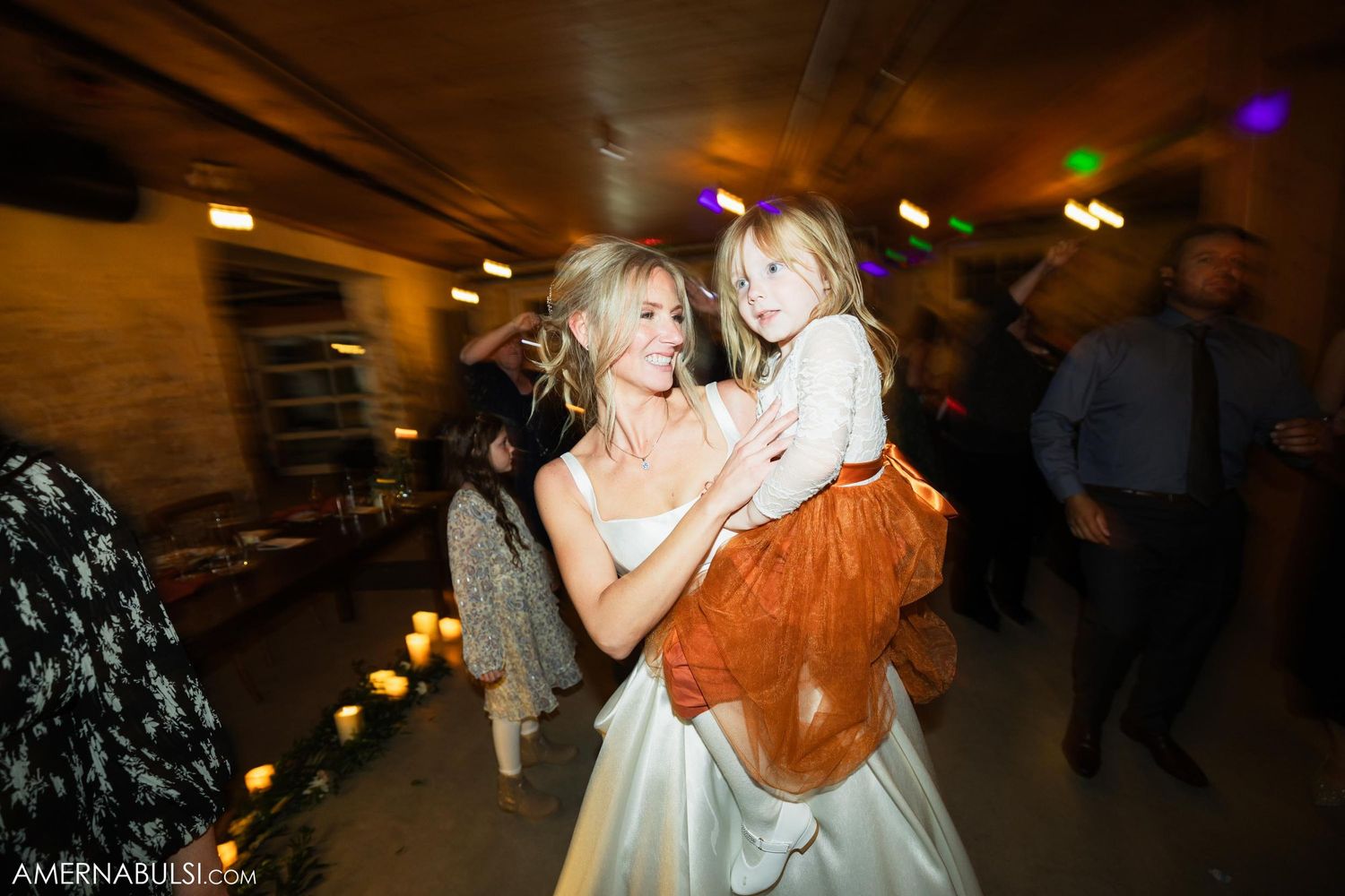 Wedding reception dance party in dimly lit venue with colorful lights.