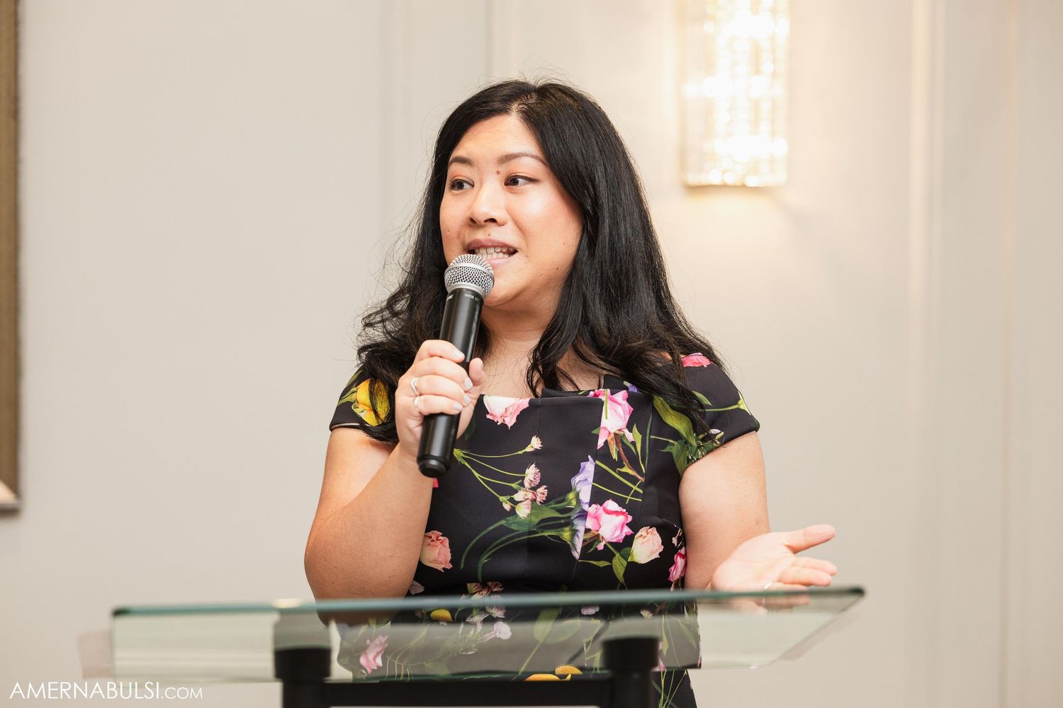 Speaker in floral dress delivers speech at wedding reception podium.