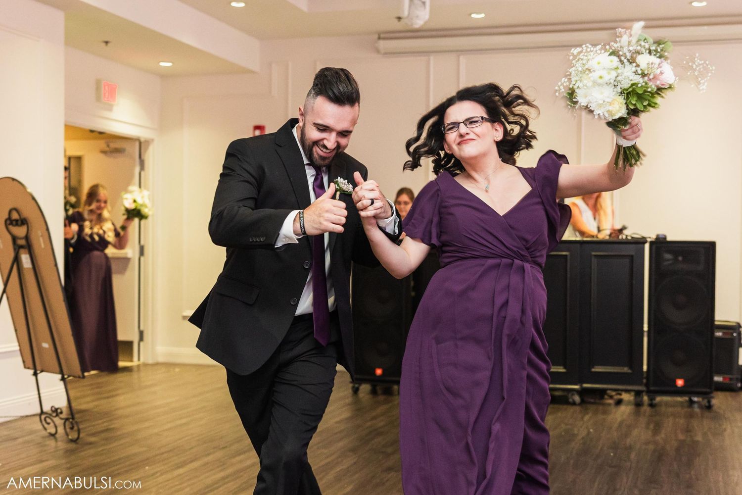 Wedding party couple dancing energetically in formal attire at reception.