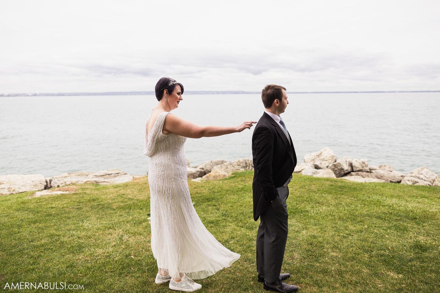 Couple participates in first look ceremony on grassy waterfront during their wedding day.