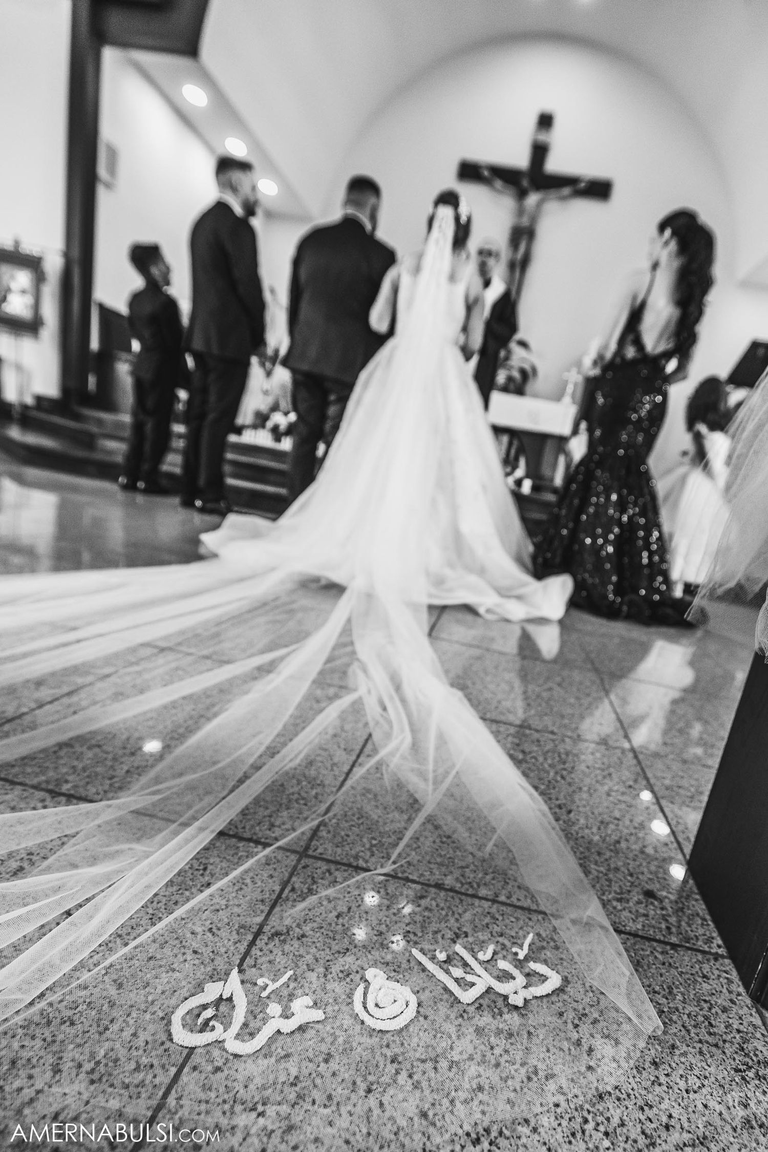 Black and white photo of a wedding ceremony in a church with a long flowing veil featuring Arabic calligraphy.