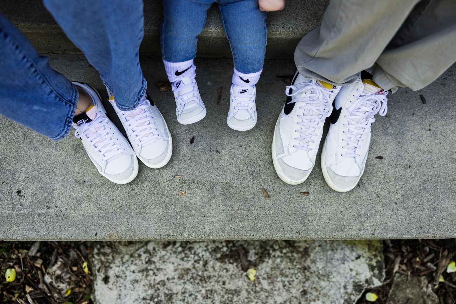 Three pairs of white sneakers photographed from above on concrete surface.