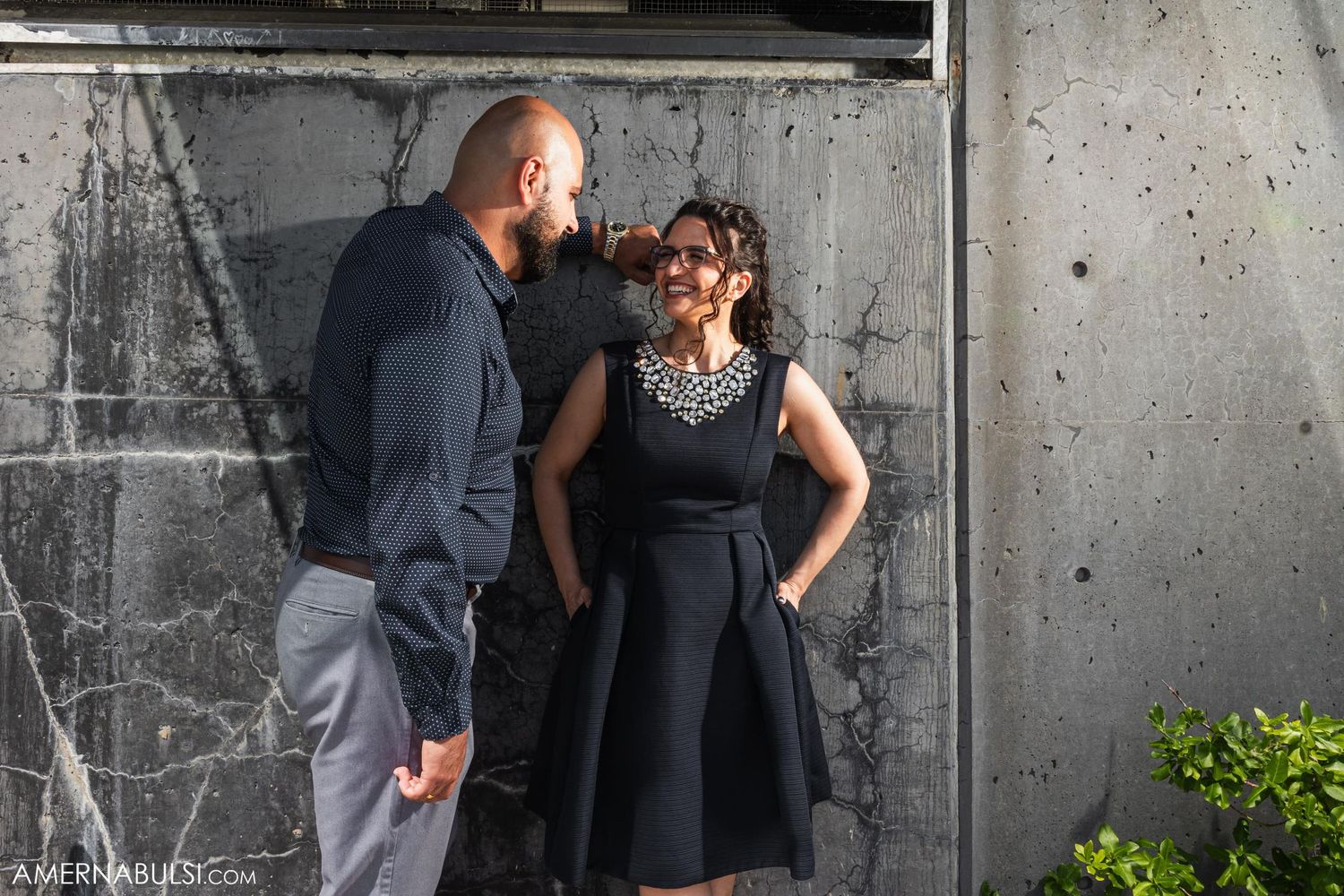 A couple poses against an industrial concrete wall during a photo session.