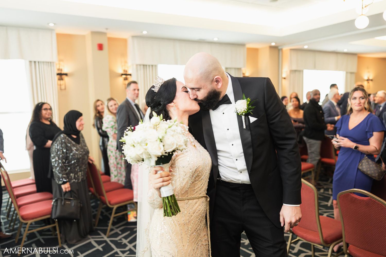 Wedding couple sharing romantic moment in reception hall with guests and floral decorations.
