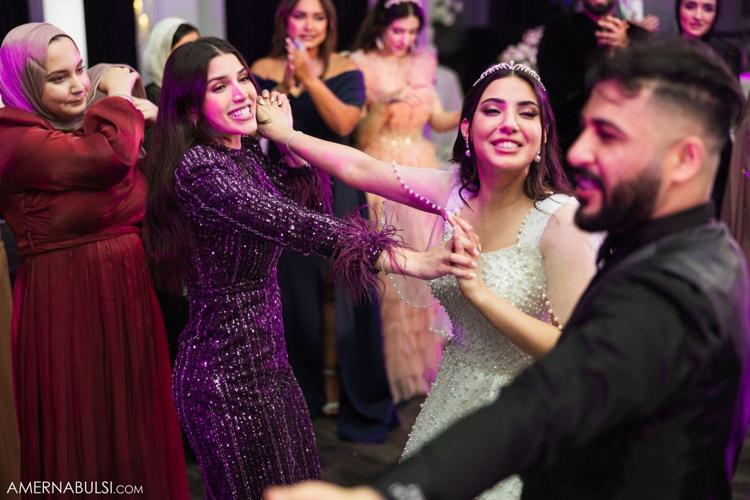 People dancing and celebrating at a wedding reception with purple lighting and festive atmosphere.