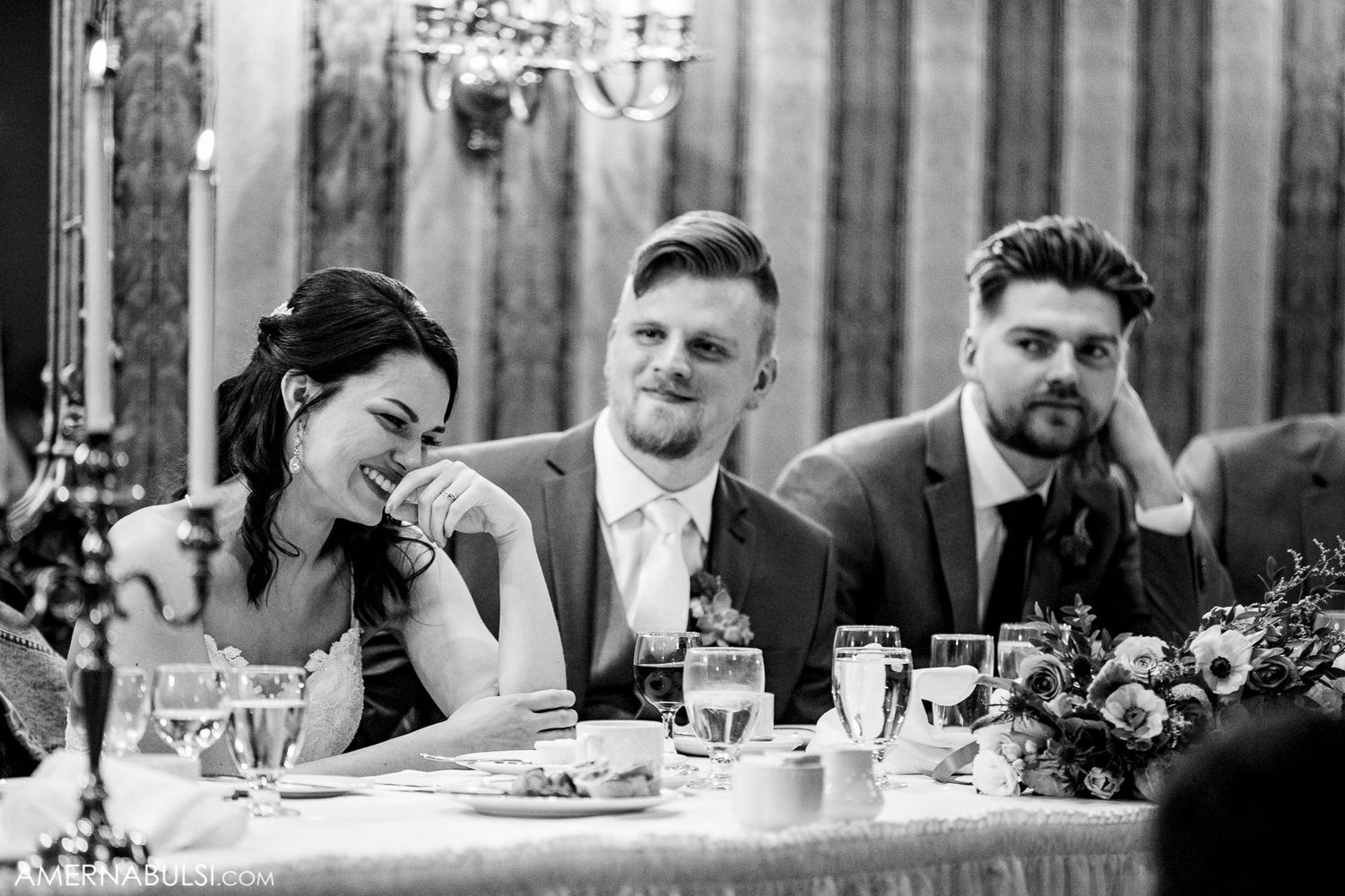 Wedding reception guests seated at long tables during dinner service in black and white.