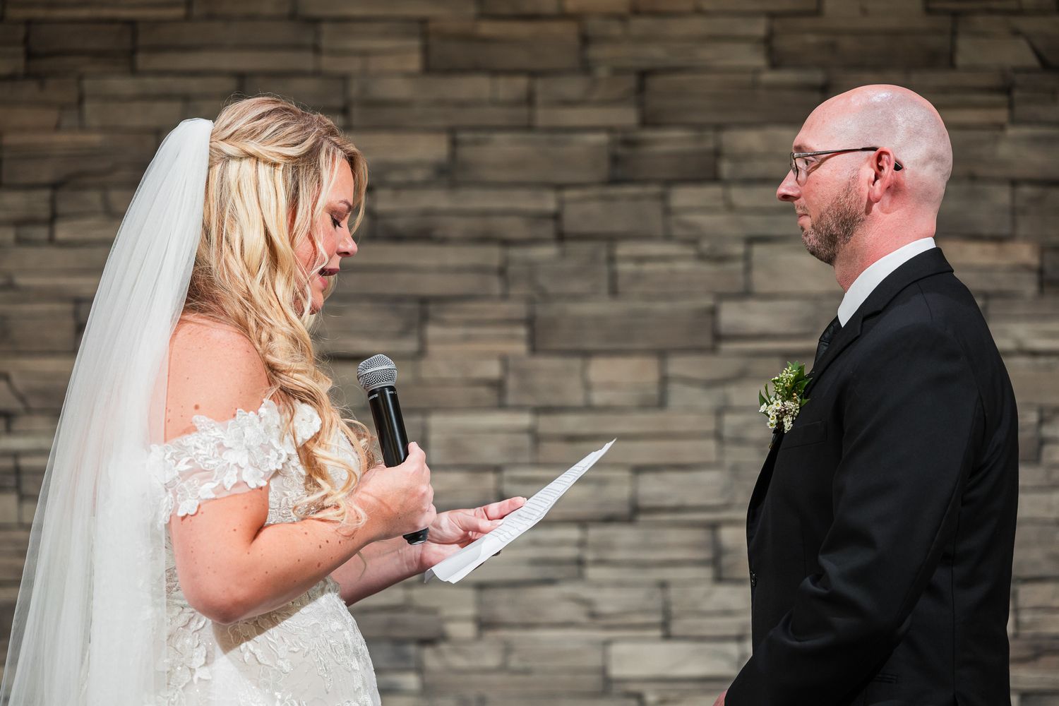 Emotional moment during wedding ceremony as couple exchanges vows against stone wall backdrop.