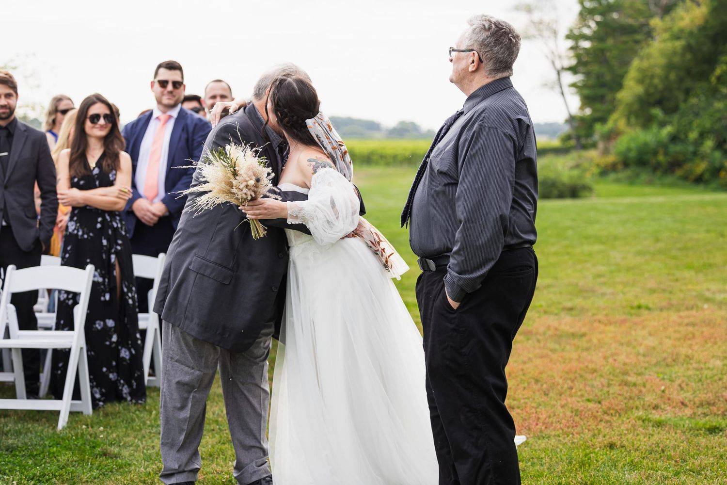 An emotional moment during an outdoor wedding ceremony with guests seated in white chairs.