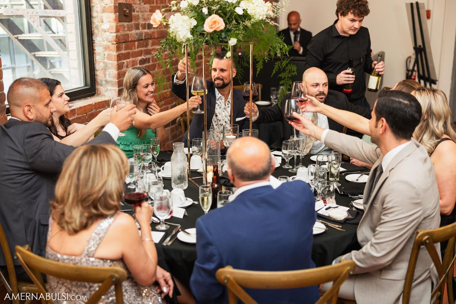 Wedding guests toasting at round tables during reception dinner celebration.