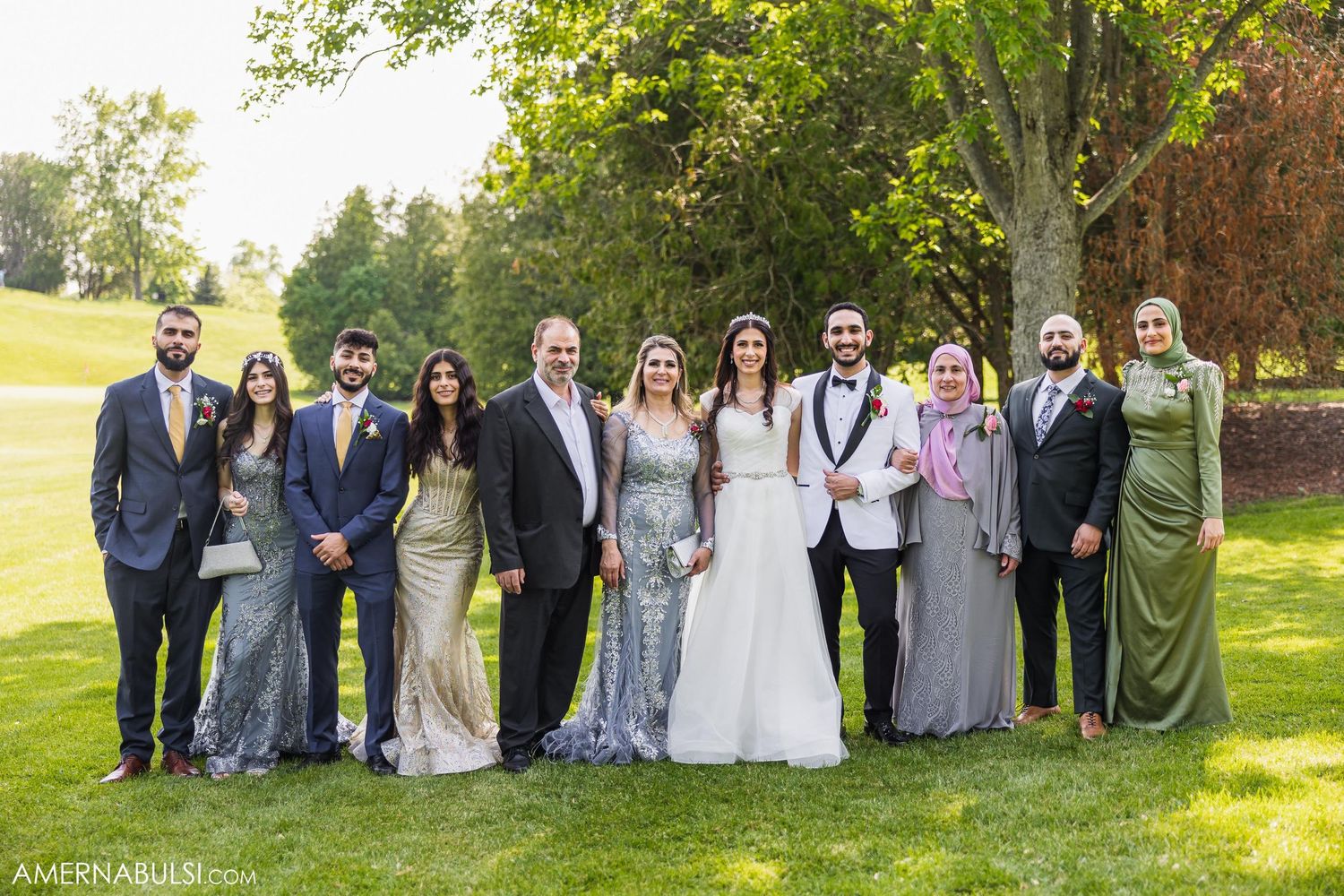 Wedding party poses for a formal group photo outdoors on a sunny day.