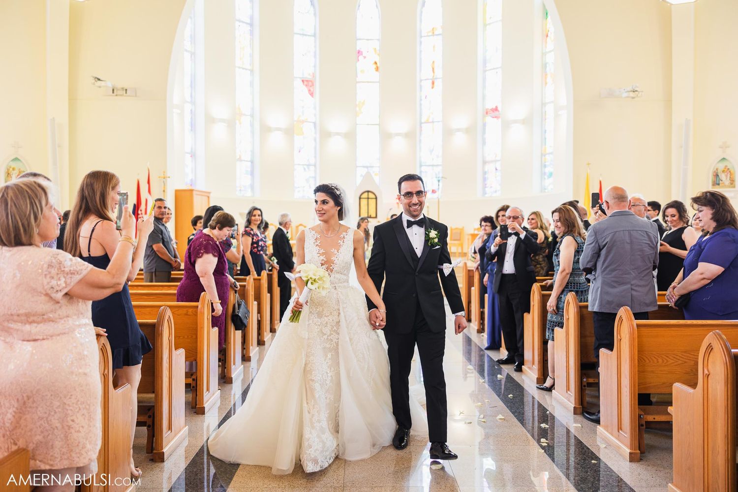 Wedding ceremony recessional with guests celebrating in church pews.