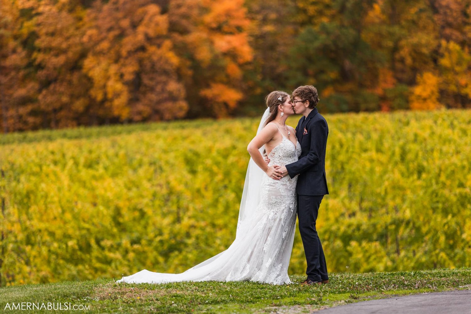 Wedding couple poses in field with vibrant orange autumn foliage backdrop.