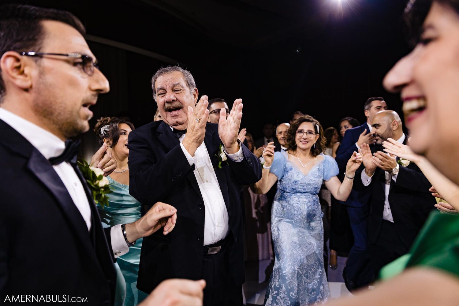 Wedding guests clap and dance during lively reception celebration.