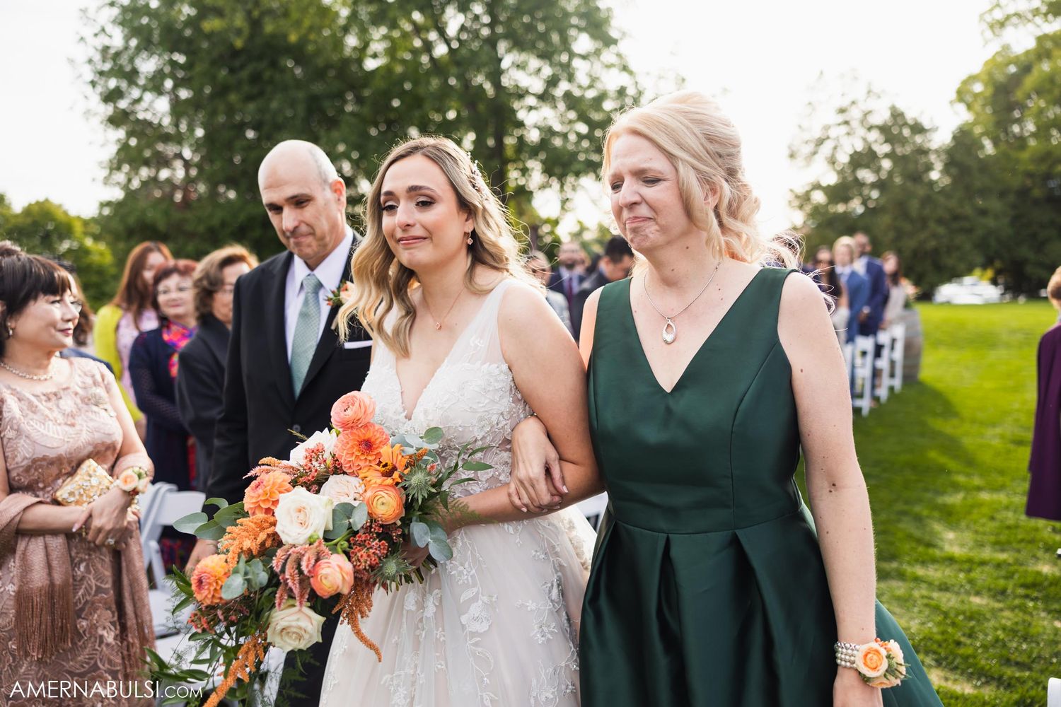 Wedding party walking through garden setting with bride holding vibrant orange and peach bouquet.