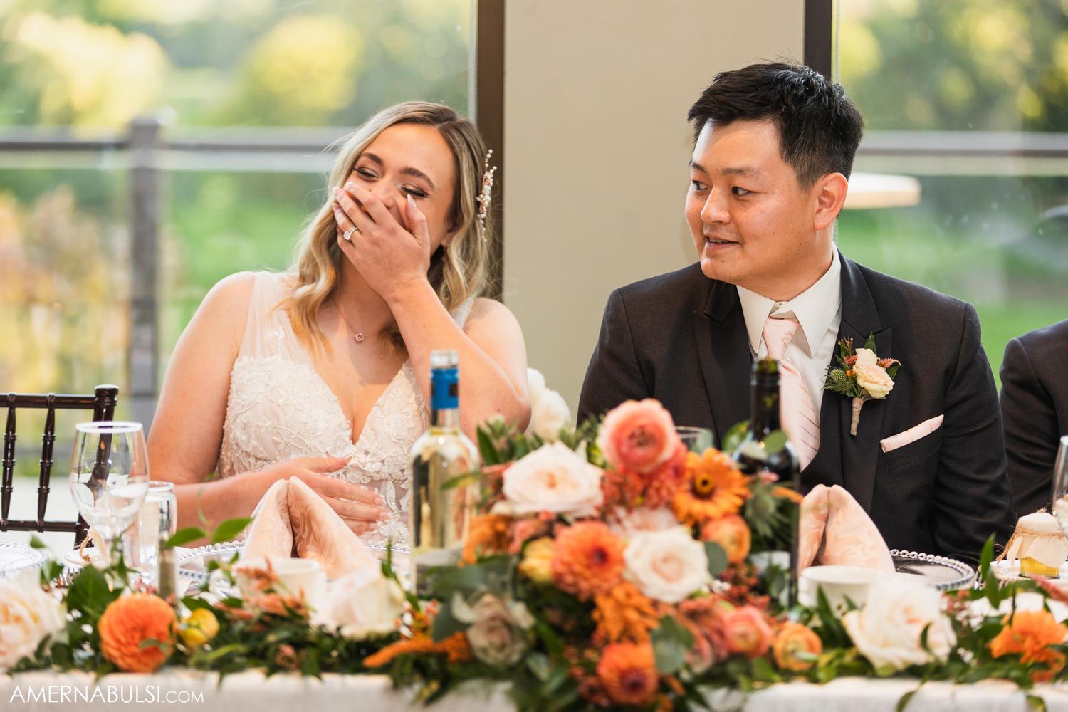 Candid moment of couple laughing at head table during wedding reception.