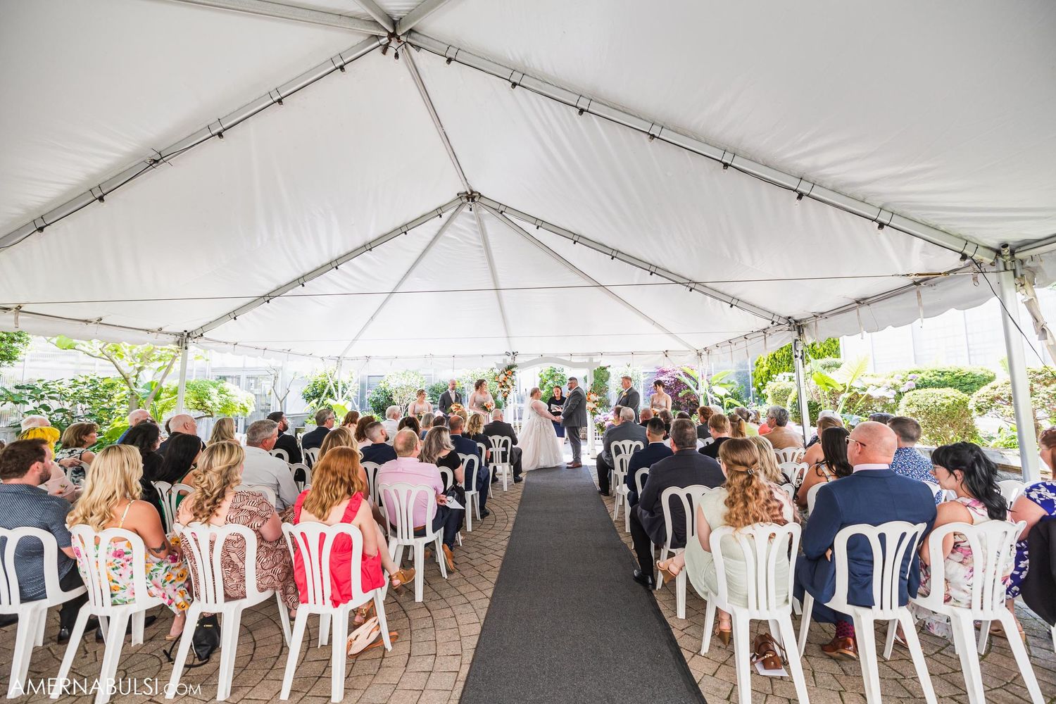 Wide view of a white tent wedding ceremony setup with rows of chairs and center aisle.