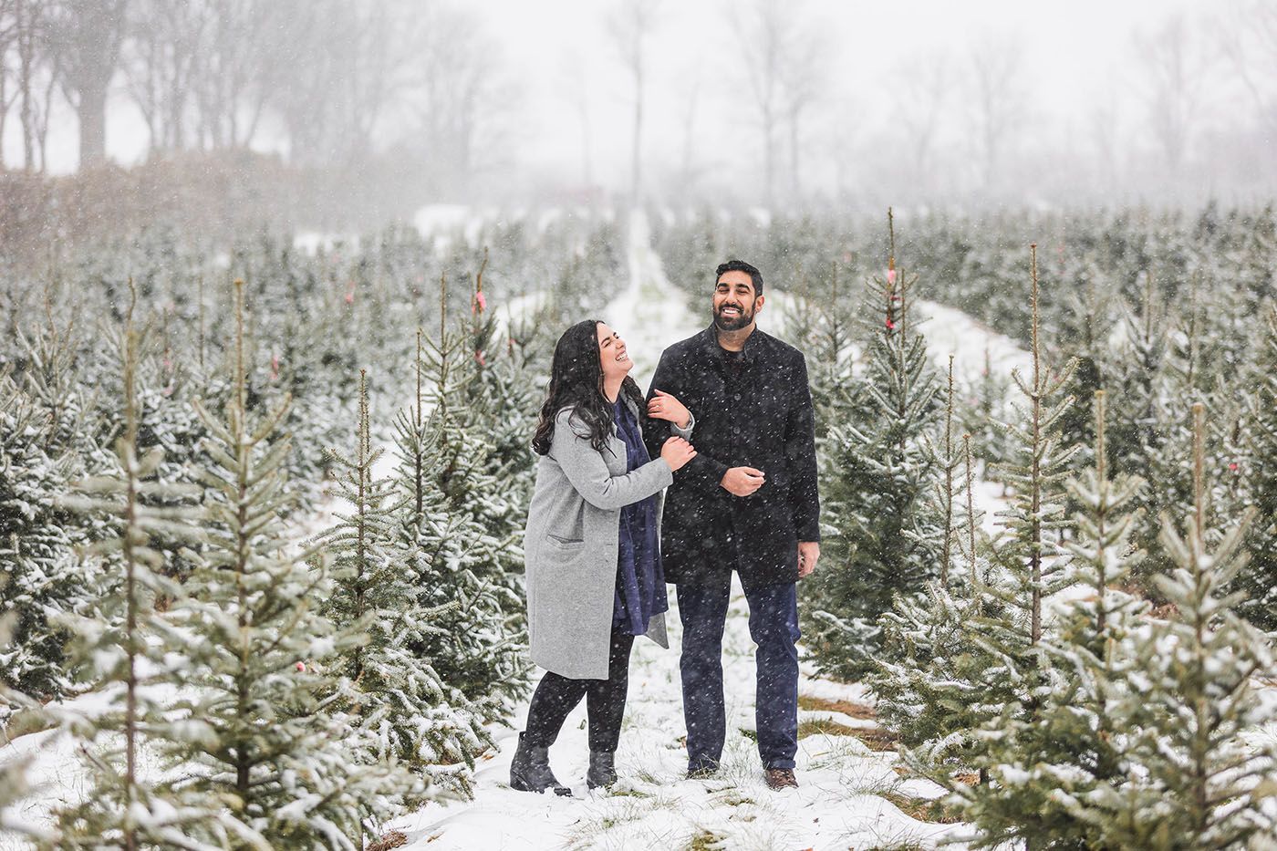 Couple walking through snow-covered evergreen trees in winter wonderland setting.