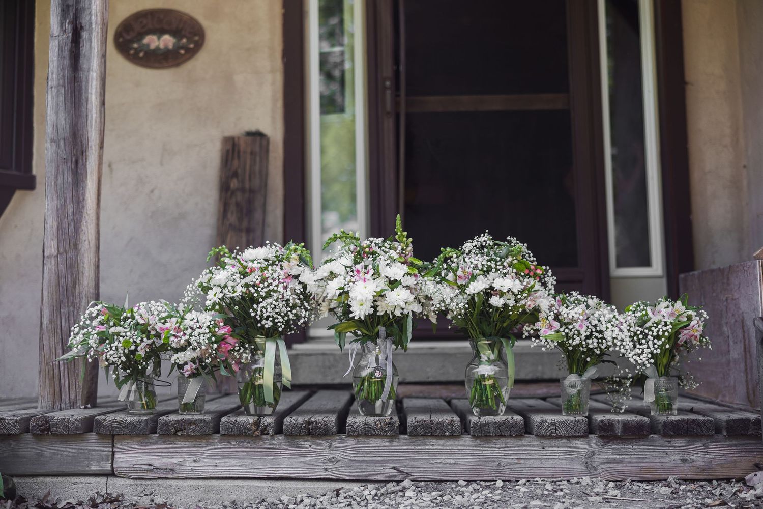 Row of mason jars with white wildflower bouquets on rustic wooden porch steps of vintage building.