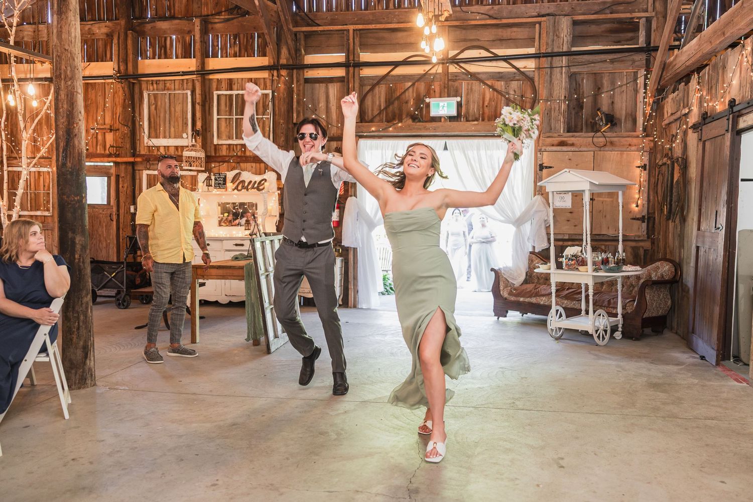 Bride and groom making grand entrance into rustic barn wedding reception with raised arms.