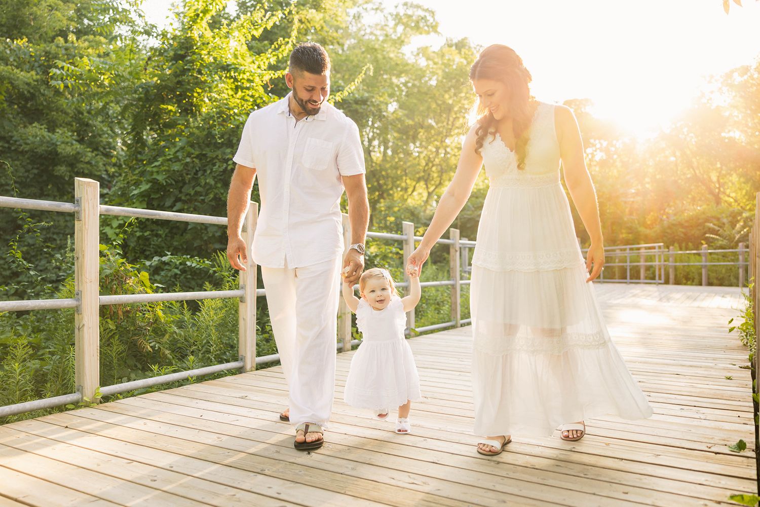 A couple in white outfits walking on a wooden boardwalk during golden hour.