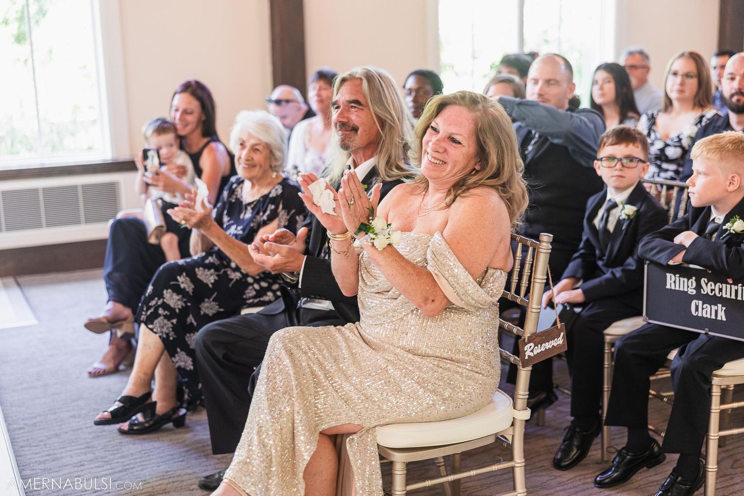 Wedding guests seated in formal attire applaud during ceremony.