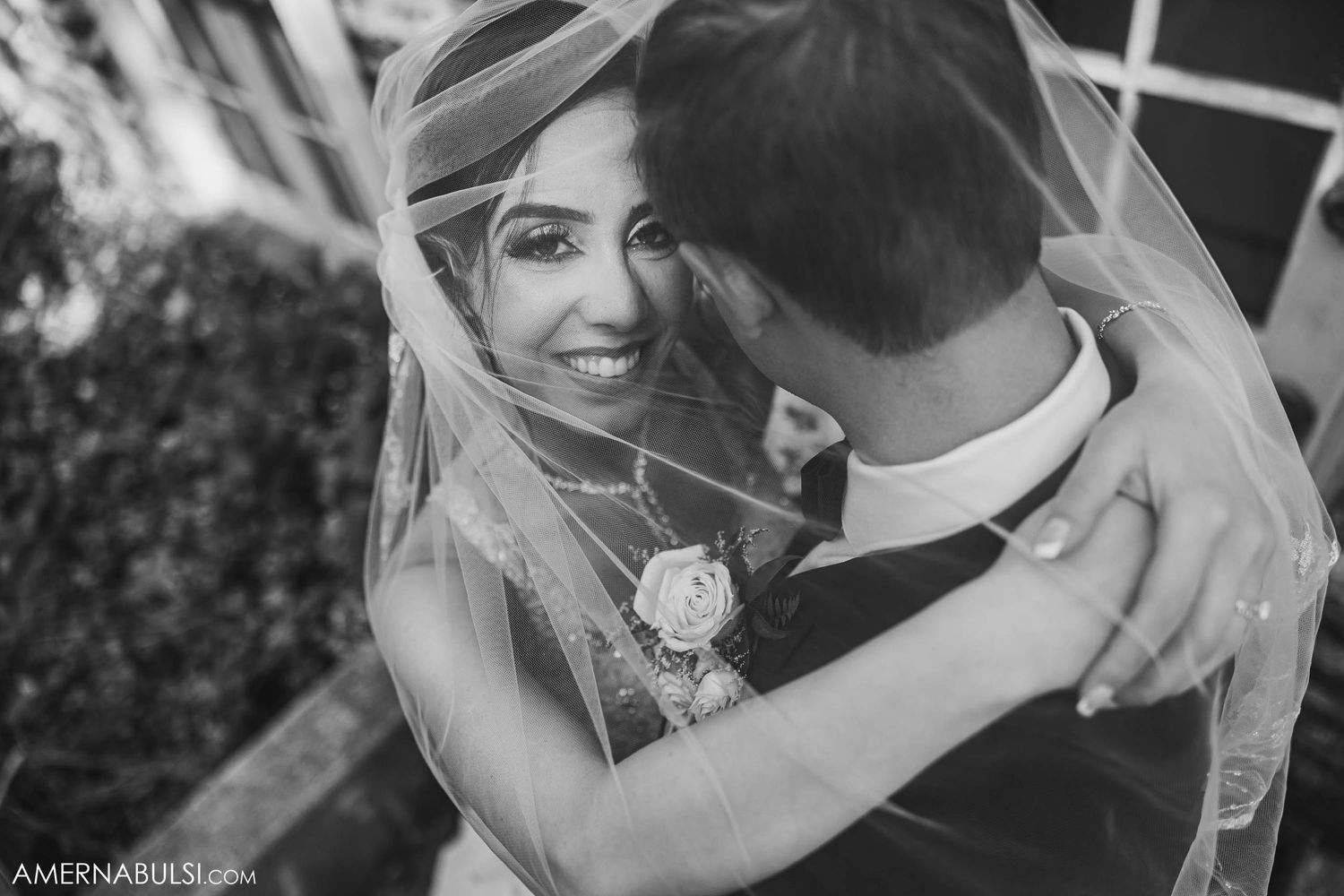 Black and white portrait of a couple embracing during their wedding with bride's veil flowing.
