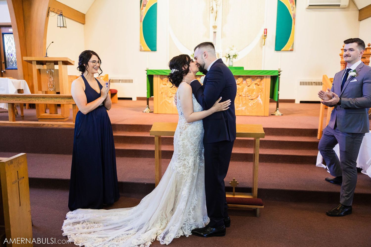 Newlyweds share first kiss at church altar while wedding party looks on.
