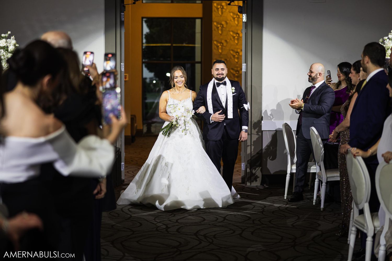 A bride and groom make their grand entrance through elegant double doors at their wedding reception.
