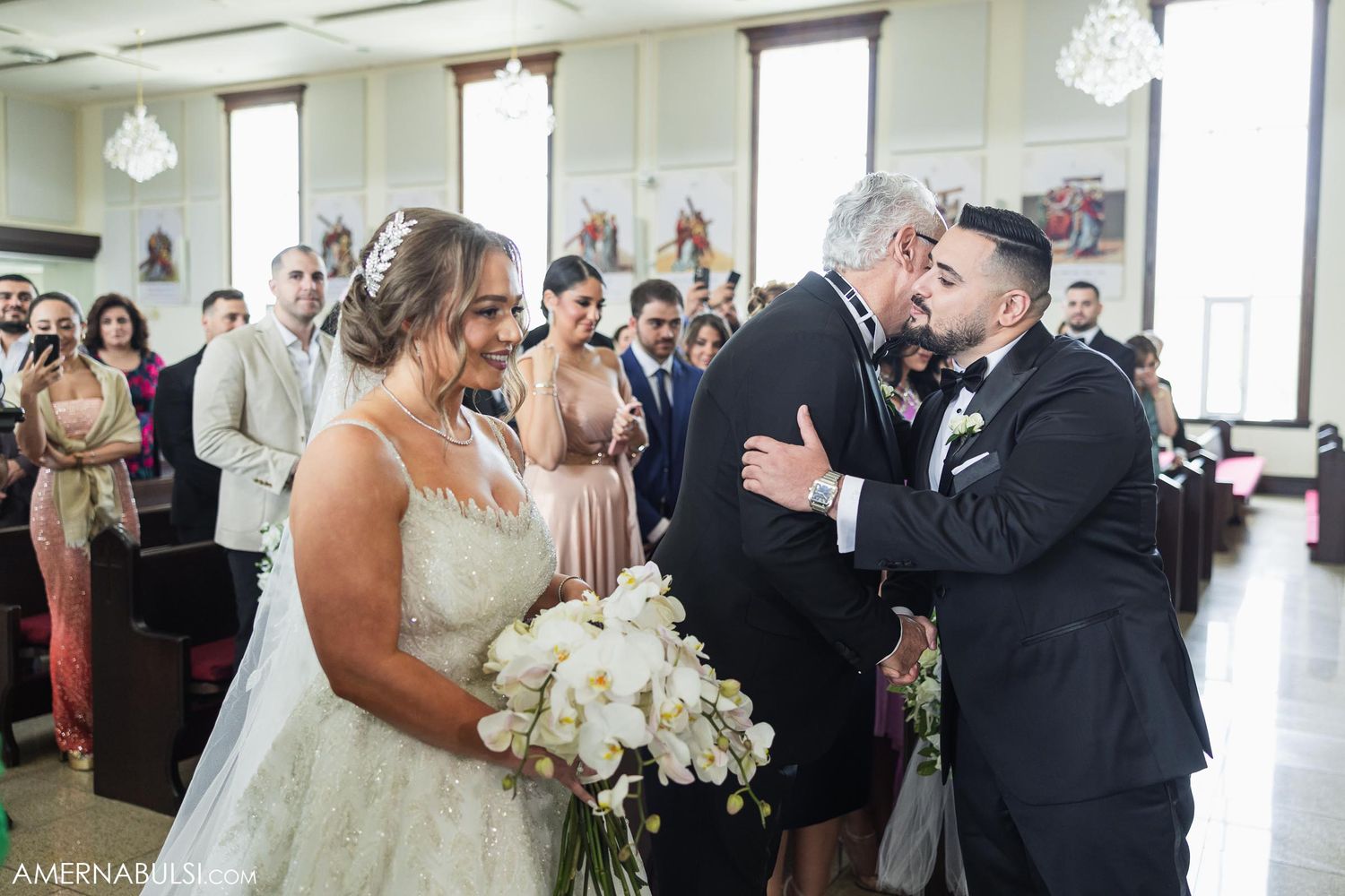 Emotional wedding moment captured in an ornate reception hall with crystal chandeliers.