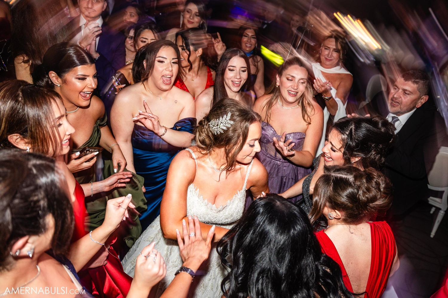 Wedding reception dance floor filled with guests in formal attire under colorful lighting.