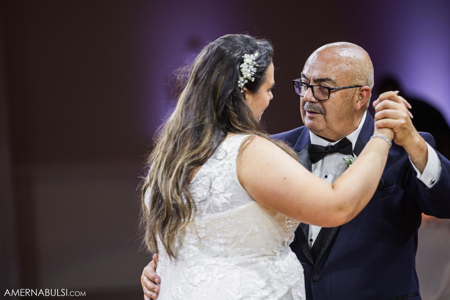 A bride in white dress dancing with an older gentleman in a tuxedo at a wedding reception.