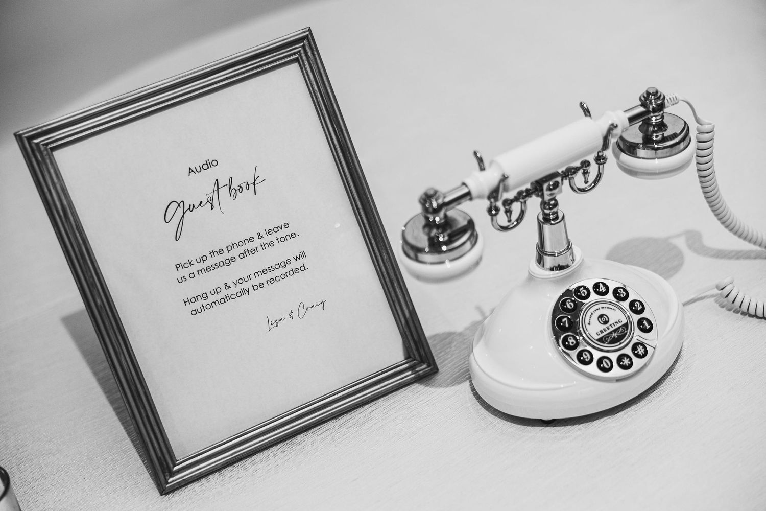 Black and white photo of vintage rotary telephone next to framed wedding guestbook sign.