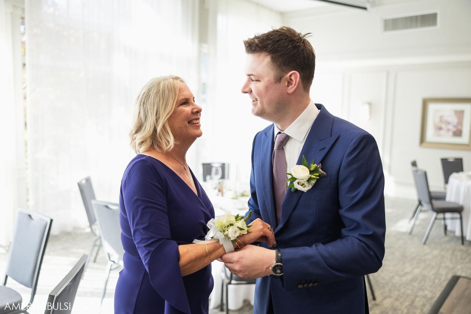 A couple in formal attire share a joyful moment while exchanging flowers indoors.