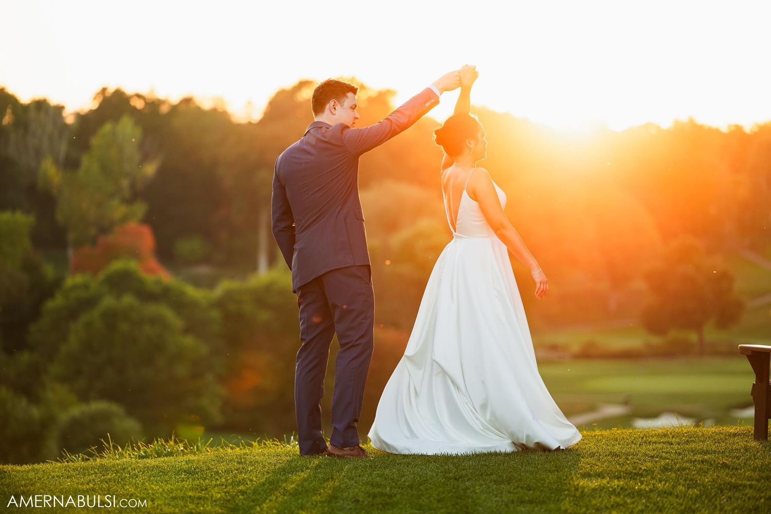 Newlyweds dance together during golden hour on a golf course.