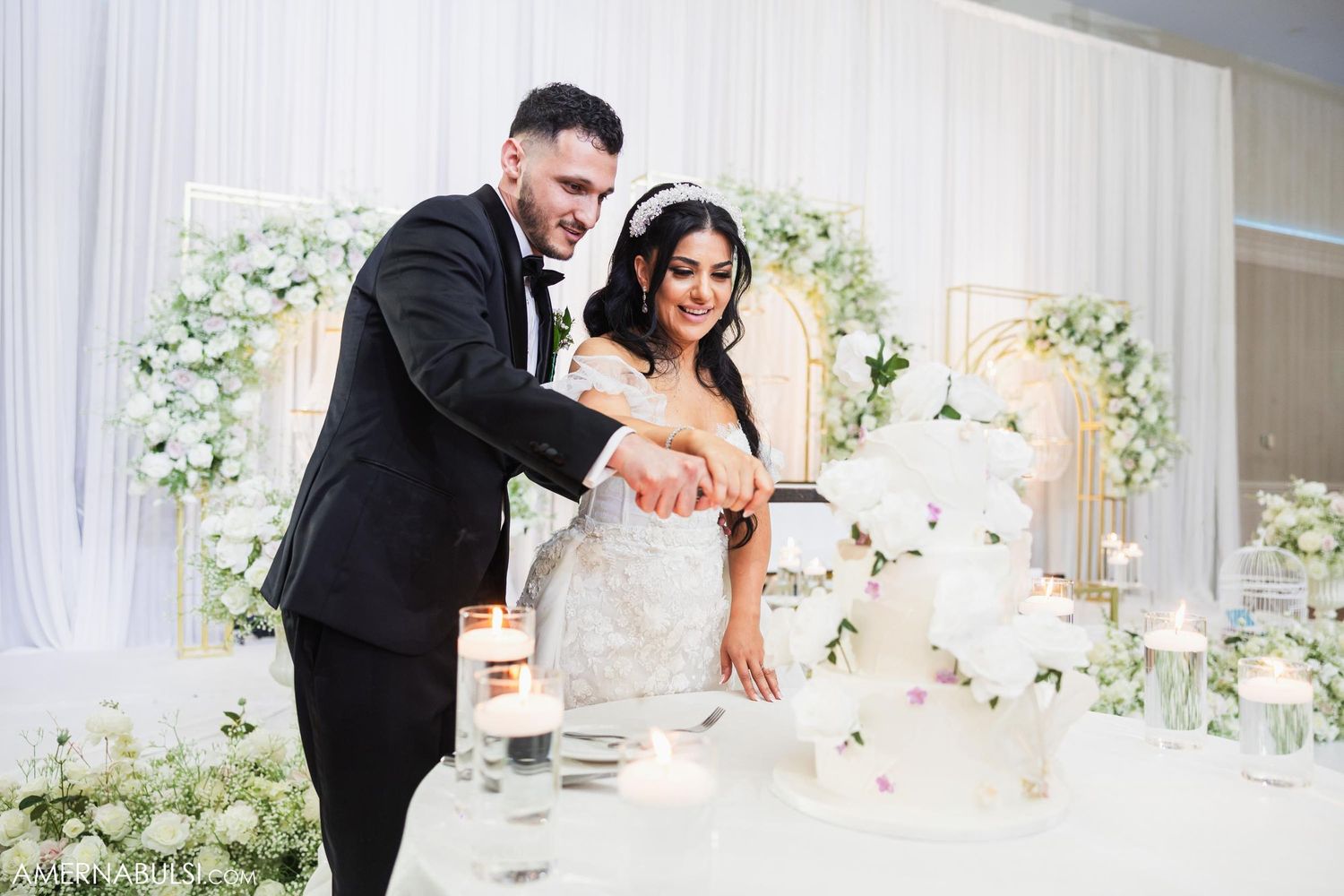 Newlyweds cut their elegant white wedding cake together at their reception.