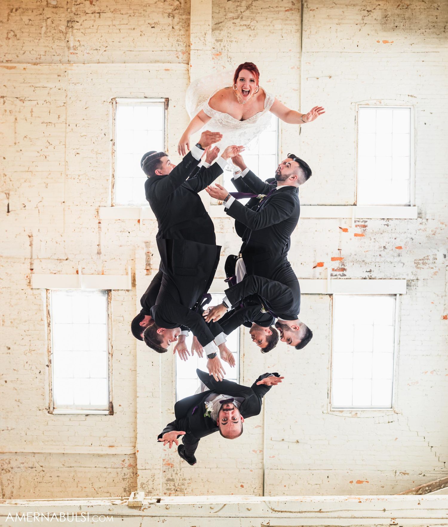 Creative wedding party photo with groomsmen lifting and posing in industrial space.