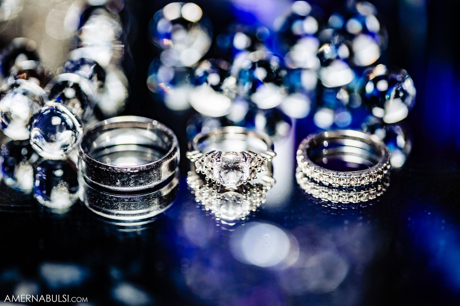 Close-up of sparkling diamond wedding rings arranged on reflective blue surface.