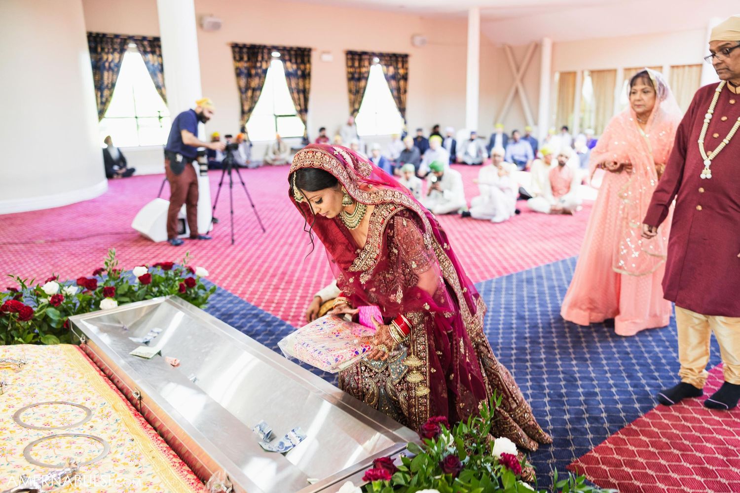 Wedding ceremony taking place on pink carpeted floor with traditional decorations and floral arrangements.