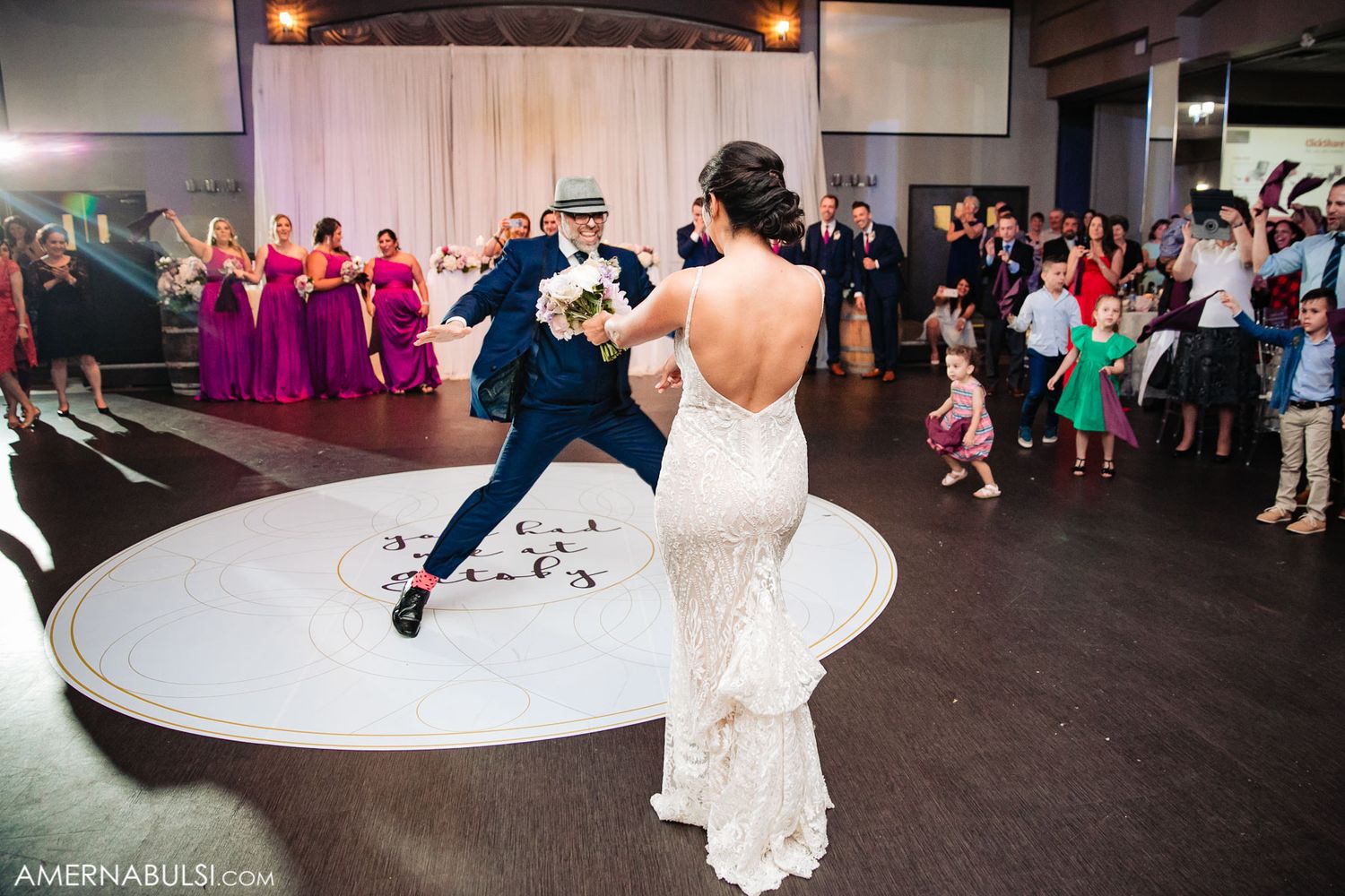 Wedding party performs choreographed dance moves in a ballroom with dramatic lighting and decor.