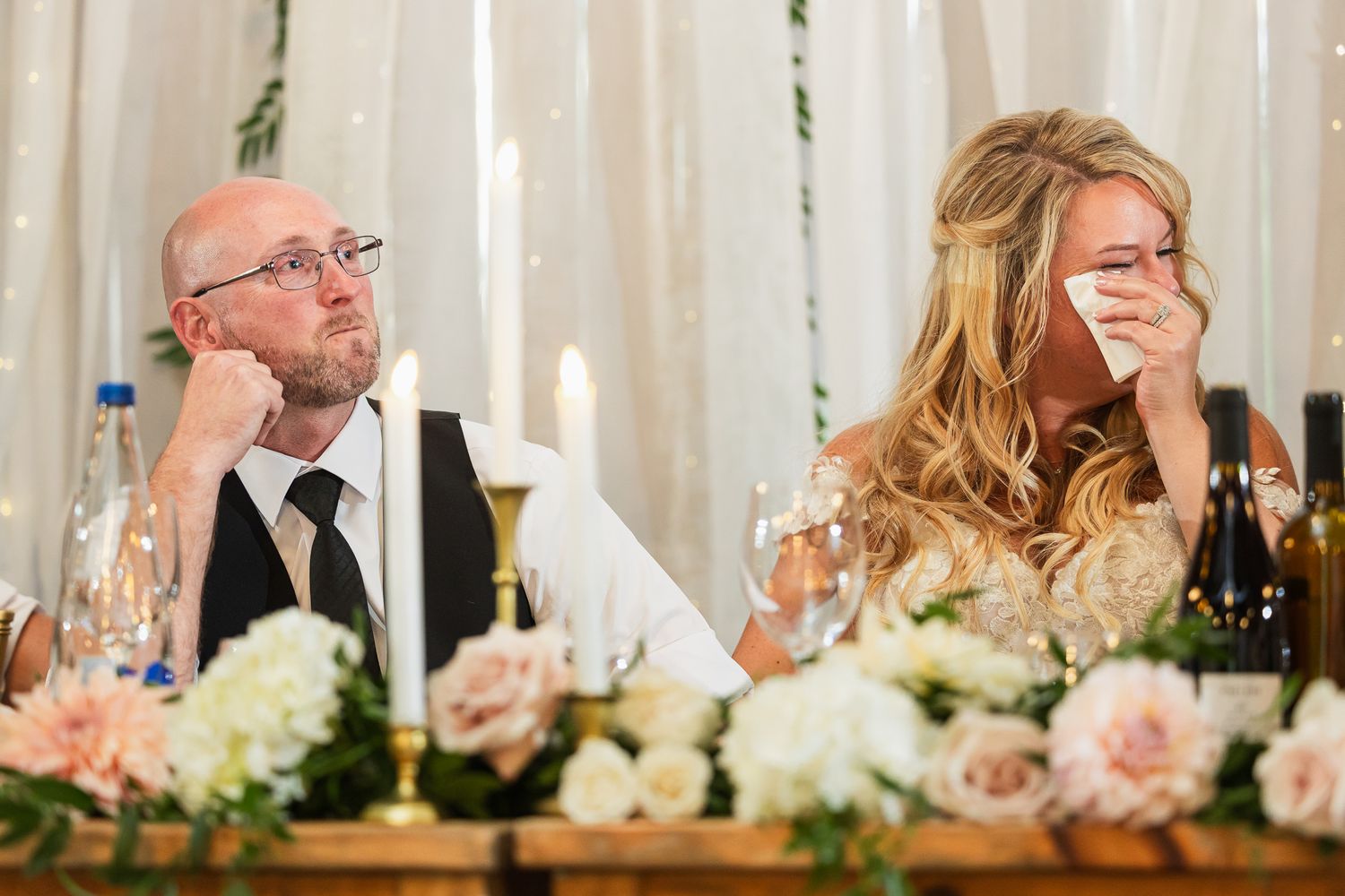 Guests seated at formal head table during wedding reception with decorative white draping backdrop.